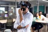 Bearded caucasian businessman wearing virtual reality simulator contemplating in modern workplace