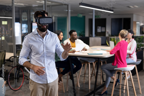 Caucasian businessman wearing vr headset against multiracial colleagues in meeting at workplace