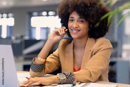 Portrait of happy african american female telecaller with headset using laptop at workplace photo