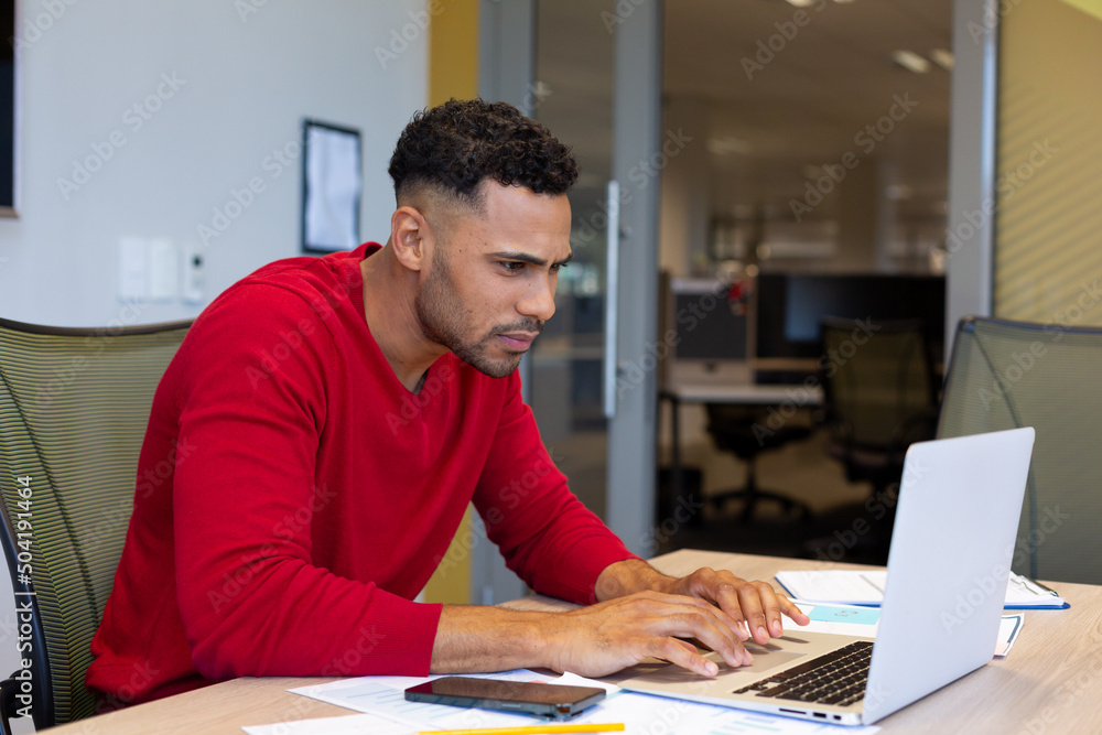 Hispanic businessman using laptop while working in boardroom at modern workplace