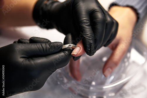 the master does a manicure to a woman with clean nails. a master in black latex gloves cuts off the cuticle on a woman's nails close-up with nail clippers photo