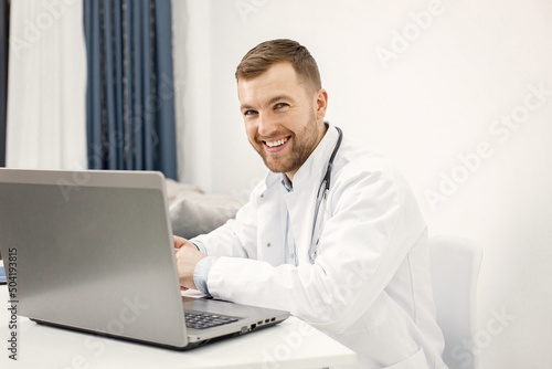 Caucasian doctor sitting at workplace and using laptop