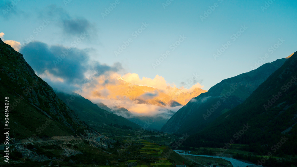 Dusk settles over the Baspa river flanked by Himalaya peaks glowing red and under blue sky. Kalpa, India.