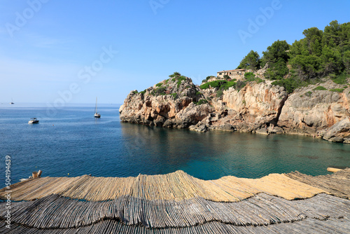 Mallorca, playa de Cala Deià, vista desde el tejado de cañizo del restaurante. Una cala de aguas cristalinas en las montañas de la Serra de Tramuntana de Mallorca. Islas Baleares, España.