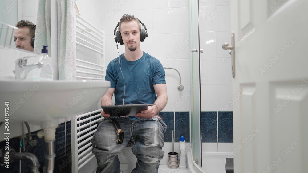 Fototapeta premium Bathroom with man watching movie on tablet with headphones