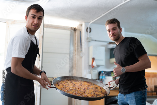 Two men with typical spanish paella in their hands.