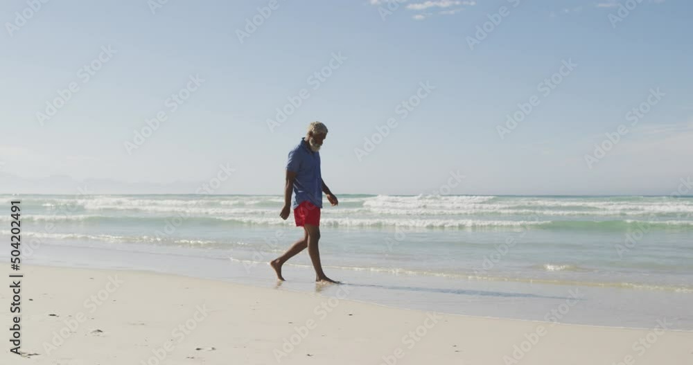 Senior african american man walking and touching water on sunny beach Senior african american man walking and touching water on sunny beach