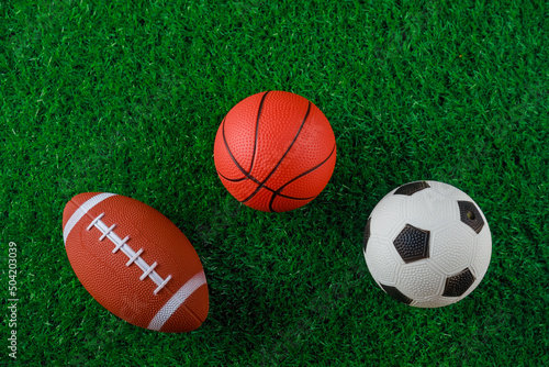 Soccer, basketball and football balls on green grass of field.
