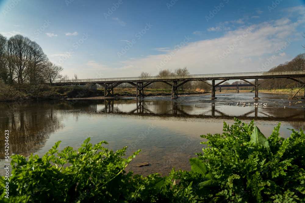 An old railway bridge crosses the smooth and gentle waters of the River Ribble near Preston, England in the United Kingdom.