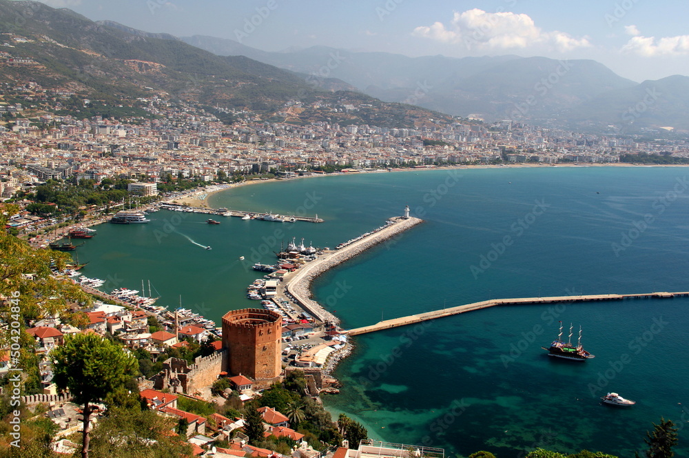 Panoramic view of Alanya city with red tower and ships in the foreground with mountains in the background in the south of Turkey