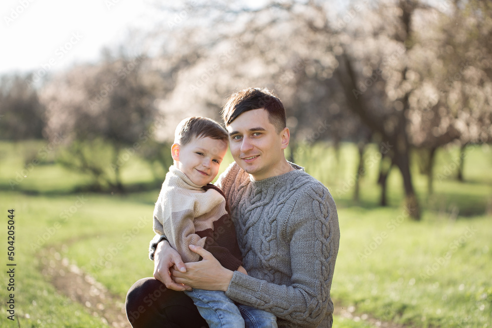 Portrait of a father and son in knitted sweaters on the background of a flowering tree in spring.