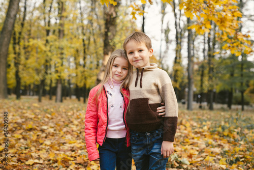 Children, a boy and a girl have fun and hug in the autumn forest among the fallen leaves