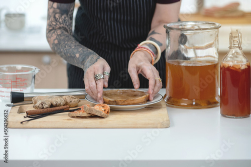 Tattooed woman holding the Scoby or fungus over plate, Scoby tea mushroom to start the fermentation process to make Kombucha, dietetic organic superfood healthy fermented tea