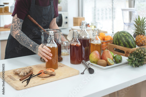 Tattooed woman preparing her kombucha tea in the kitchen, dietetic organic superfood healthy fermented tea