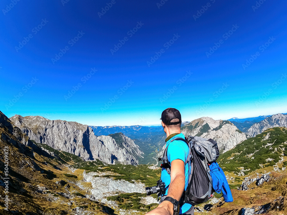 Man with backpack filming himself while hiking to the summit of Hinterer Polster in the scenic region of the Hochschwab mountain in Styria, Austria. Alpine meadows and sharp rocks. Hike concept. Free