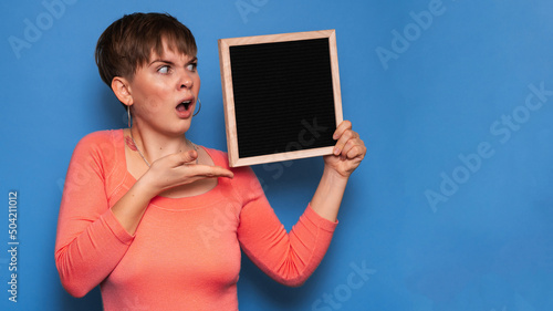 Studio shot of a young woman with a puzzled expression, holding a blank letter board on a blue background. Copy space, space for your ad or text.