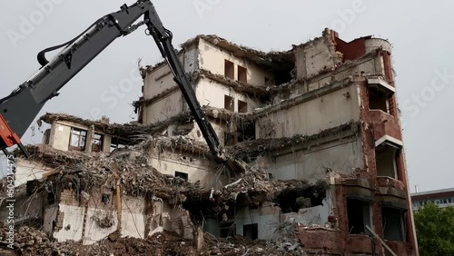 Excavator (bulldozer) demolishing a concrete building on a demolition site with debris piles. 4k mid range still shot. photo