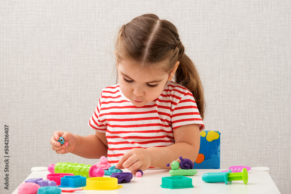 caucasian little girl plays with plasticine, modeling clay, molds, sculpting different figures on white table at home caucasian little girl plays with plasticine, modeling clay, molds, sculpting different figures on white table at home