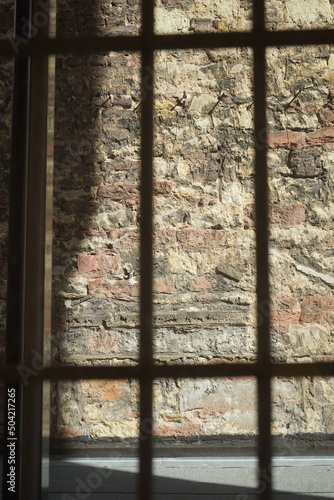 Photographie Gitter eines Fenster vor altem Mauerwerk aus Bruchstein und Naturstein in Naturf