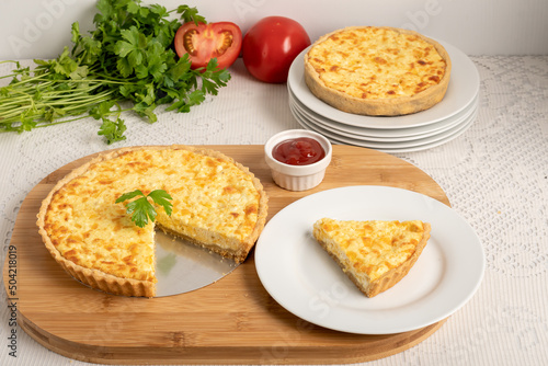 Cheese quiche, a pie on a wooden board, a slice of the pie on a white plate