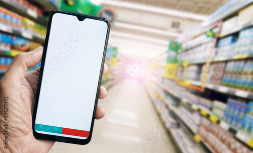 Close up view, hand holding smart phone with blank screen and basket icon and message icon  on bottom, Blurred products in shelf on background