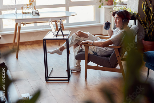 Tableau sur toile Smiling young guy listening to music with headphones and holding a cup of coffee