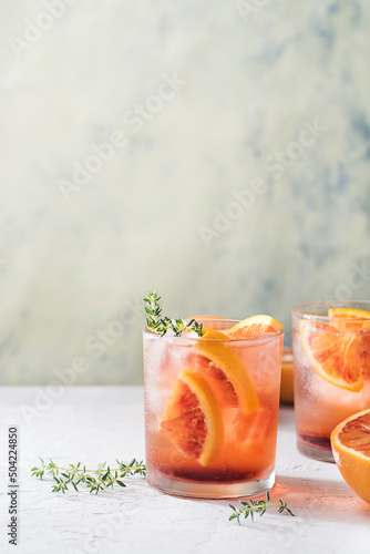 Red cocktail with Campari or bitter with  Sicilian red oranges (tarocco) on light gray concrete background, copy space. Aperitif with Americano cocktail. Natural eco  aesthetic, mint  green background