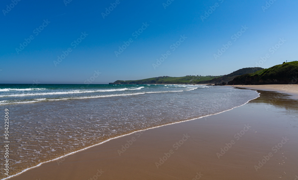 beautiful golden sand beach with gentle waves and green cliffs in the background