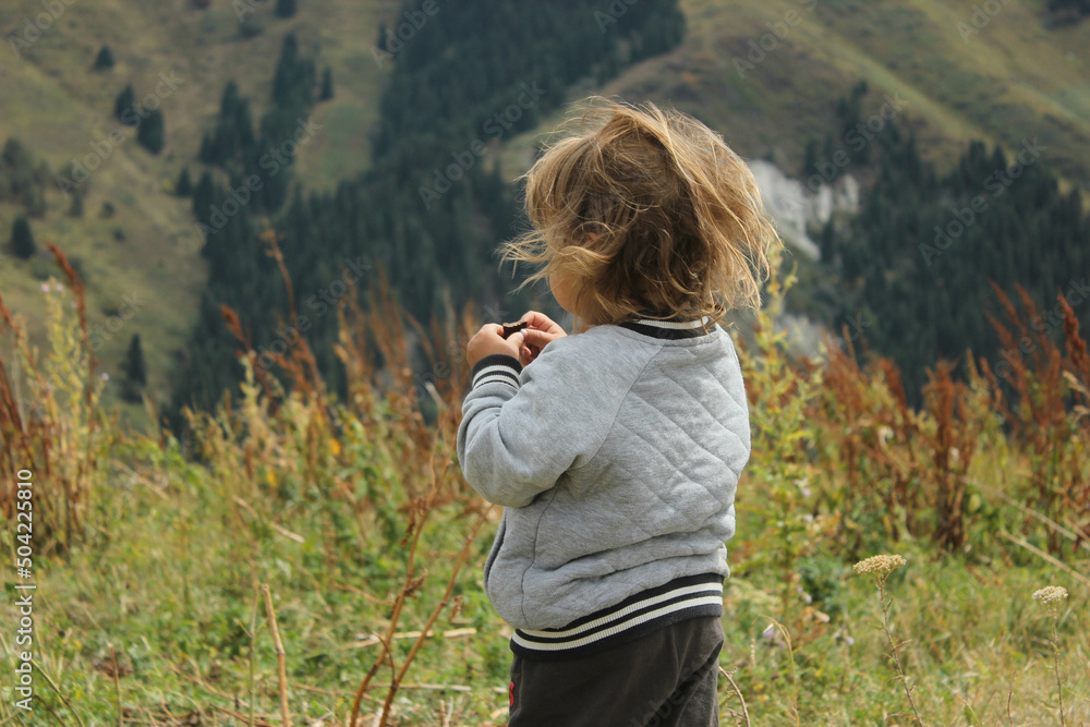 Beautiful mountains landscape in mountains, and boy with long hair. Child watching on the field and mountains. Beautiful mountains landscape in mountains, and boy with long hair. Child watching on the field and mountains.
