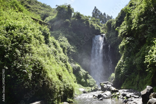 View of Peguche Waterfall in the mountains. It's surrounded by green forest full of vegetation. Ecuador