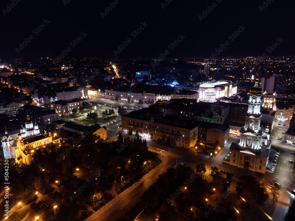 Night lights illuminated city aerial view. City center square (Maidan Konstytutsii) with Dormition Cathedral, Svyato-Pokrovskyy Monastyr landmarks in Kharkiv, Ukraine