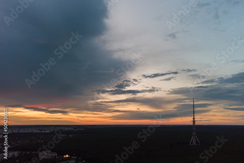 Aerial sunset evening view on telecommunication tower antenna in forest near residential district and scenic cloudy sky. Kharkiv city, Ukraine
