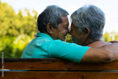 Close-up of smiling biracial senior couple looking at each other while sitting on bench in park