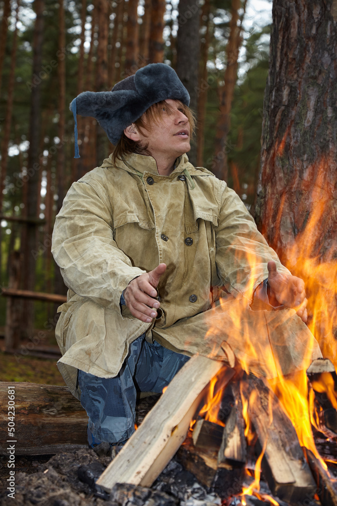 A man is sitting near a campfire. A man in the forest lit a fire.