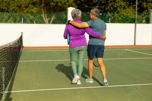 Rear view of biracial senior husband and wife with arms around walking at tennis court on sunny day © WavebreakMediaMicro