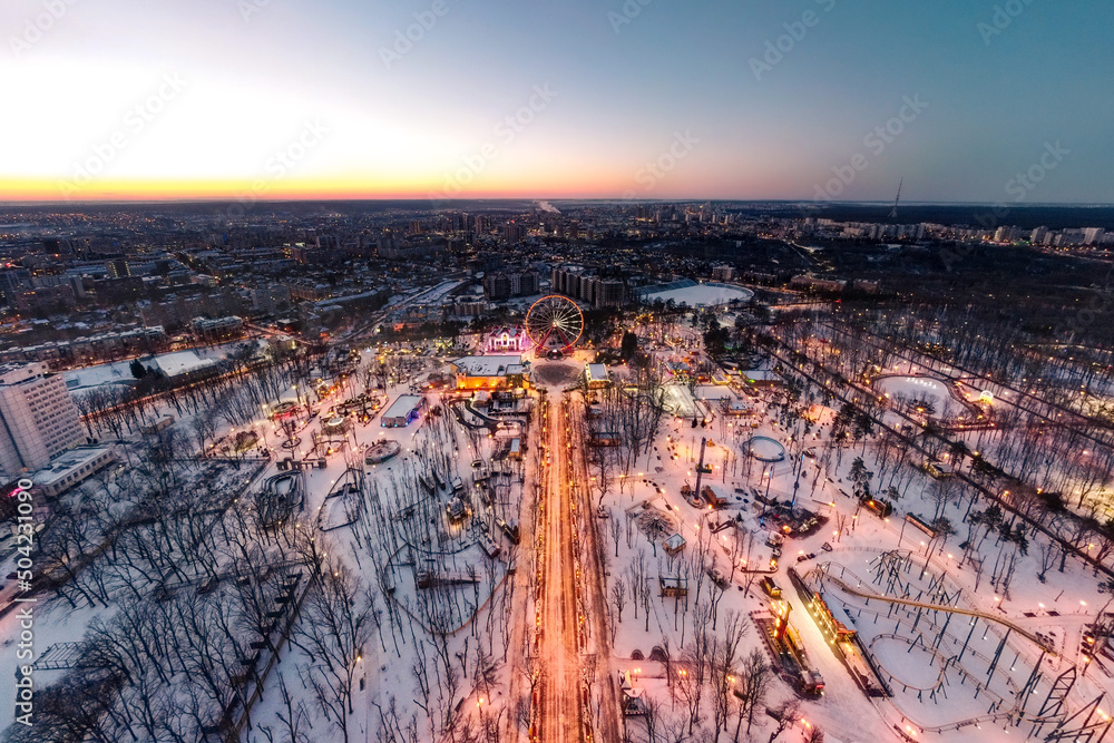 Aerial view on illuminated Ferris wheel and attractions in amusement Gorky Central Park at sunset. Winter wide angle cityscape panorama in Kharkiv