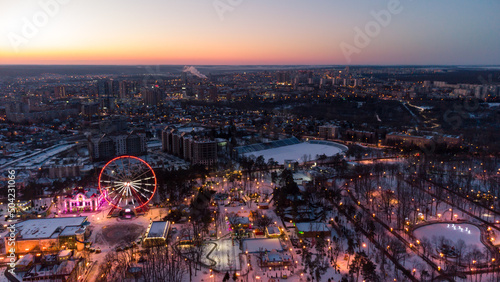Aerial panorama on vivid evening cityscape, Ferris wheel and entertainments in winter, covered in white snow. Kharkiv city center in sunset colors, amusement Gorky Central Park © Kathrine Andi