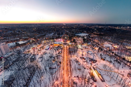 Aerial view on illuminated Ferris wheel and attractions in amusement Gorky Central Park at sunset. Winter wide angle cityscape panorama in Kharkiv