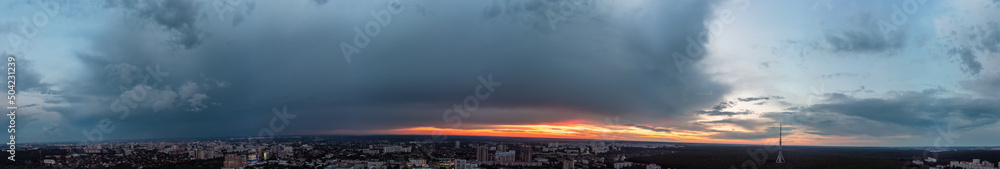 Dramatic ultra wide sunset cloudscape panorama view in city residential district. Aerial Pavlovo Pole, Kharkiv Ukraine. Evening skyscape, cloudscape with heavy dark clouds and orange sun