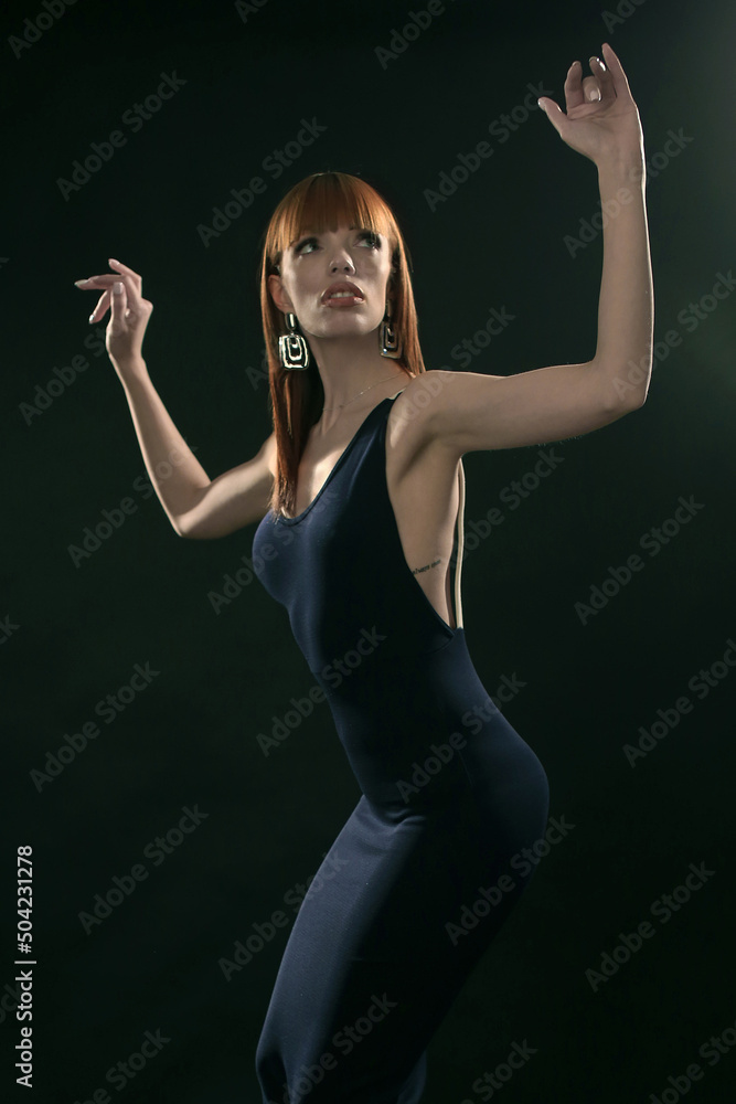 Portrait of a red-haired fashionista in the studio, dressed in a black dress on a black background