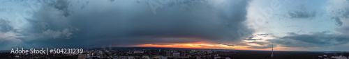 Dramatic ultra wide sunset cloudscape panorama view in city residential district. Aerial Pavlovo Pole, Kharkiv Ukraine. Evening skyscape, cloudscape with heavy dark clouds and orange sun
