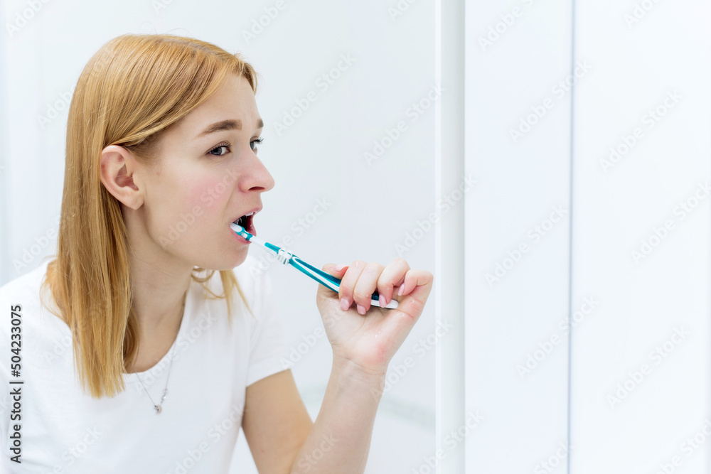 Young and cheerful woman brushing teeth with toothbrush during morning hygiene procedures in the bathroom Young and cheerful woman brushing teeth with toothbrush during morning hygiene procedures in the bathroom