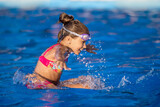 A girl with swimming goggles jumps into a pool with clear water on the background of a warm summer sunny sunset