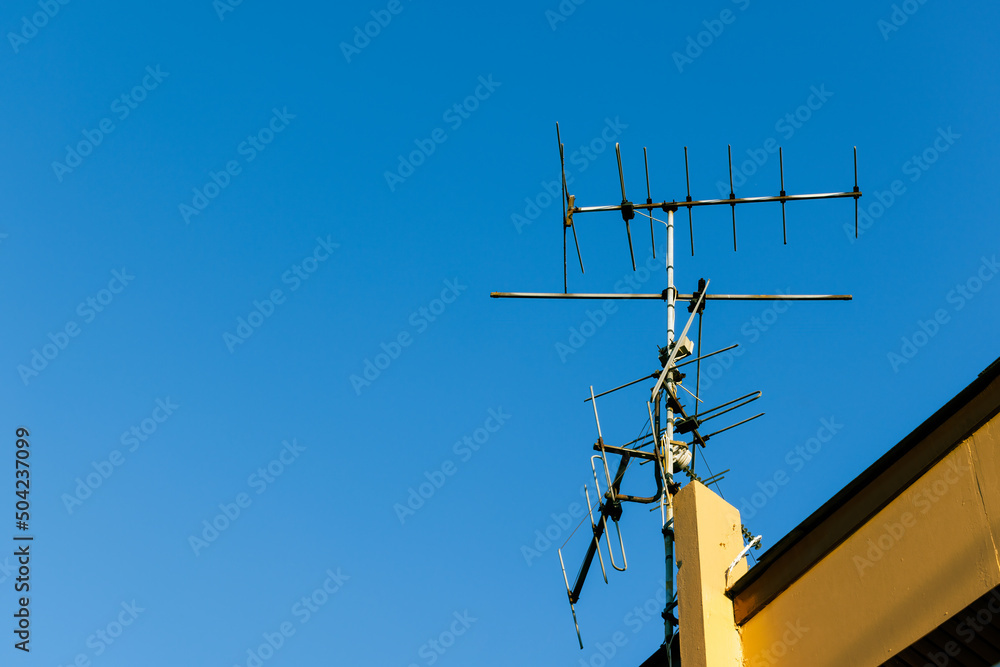 Old analog television aerial transmission antenna on the roof of house in clear blue sky. Obsolete tv and radio communication and broadcasting technology. Old analog television aerial transmission antenna on the roof of house in clear blue sky. Obsolete tv and radio communication and broadcasting technology.