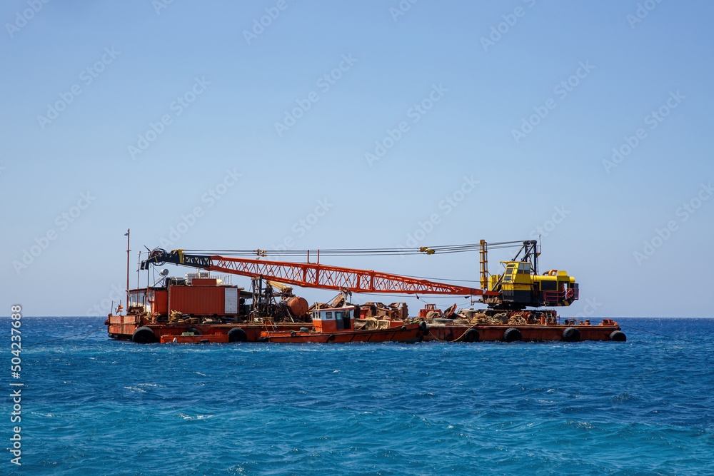 Construction barge with a crane in blue sea.
