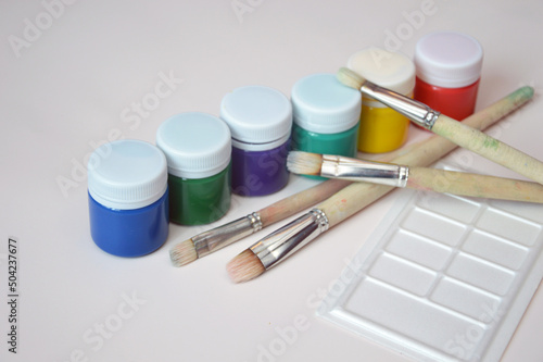 Multi-colored gouache paint in closed jars and a set of artistic brushes. Drawing materials, hobbies, tools, artist's palette.