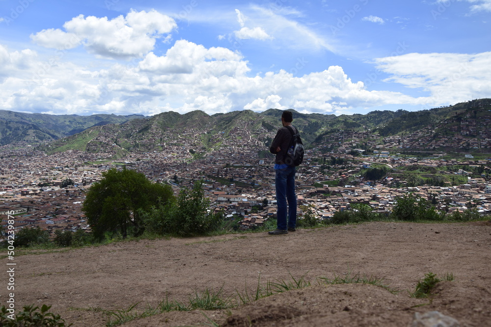 A man stands in the ruins of saqsaywaman, and look at the city of Cusco