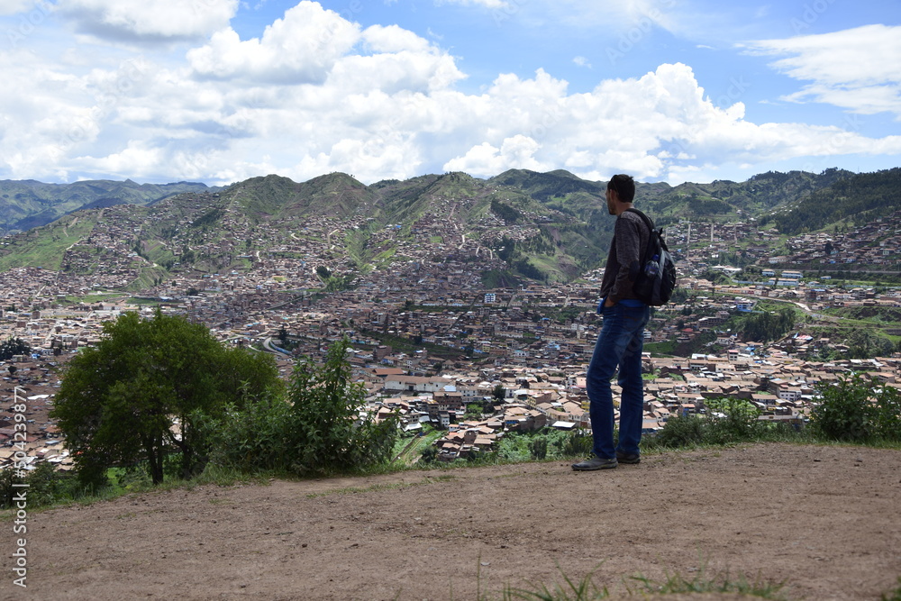 A man stands in the ruins of saqsaywaman, and look at the city of Cusco