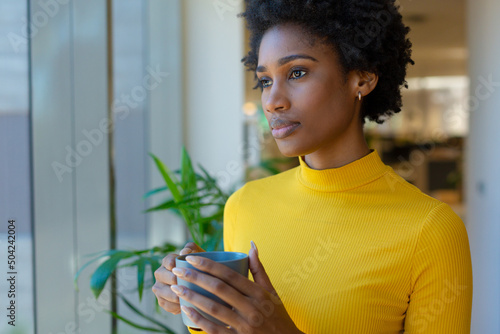 Beautiful young african american businesswoman holding coffee mug contemplating at modern workplace