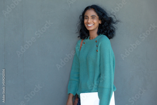 Happy beautiful young biracial businesswoman with tablet pc standing against gray wall at workplace